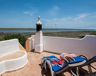 Rooftop terrace with lounge chairs overlooking coastal wetlands and water under a clear blue sky.